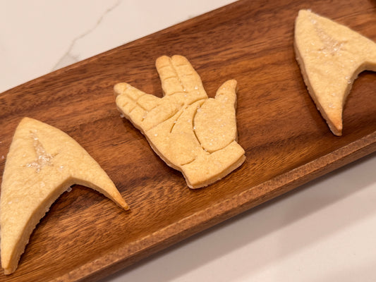Three cookies shaped like the vulcan hand, star trek emblem logo, on a board